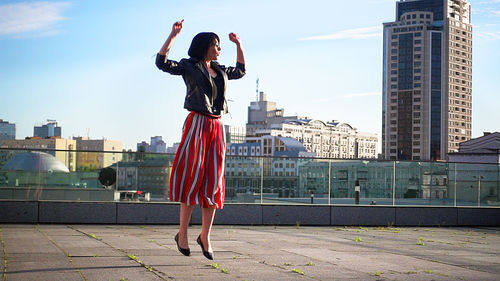 Happy woman wearing striped skirt and jacket on footpath in city