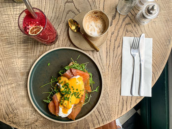 Eggs benedict with salmon and rocket on toast with latte or cappuccino coffee and red berry smoothie