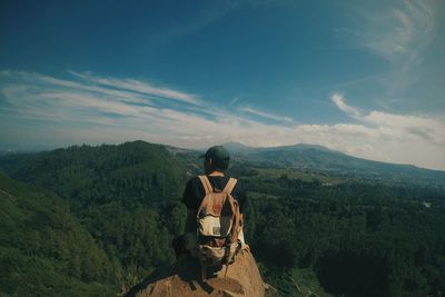 Rear view of man sitting against mountains on rock