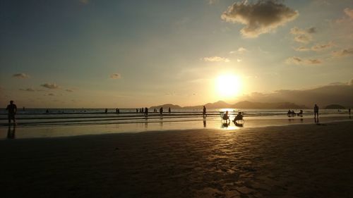 Silhouette people on beach against sky during sunset