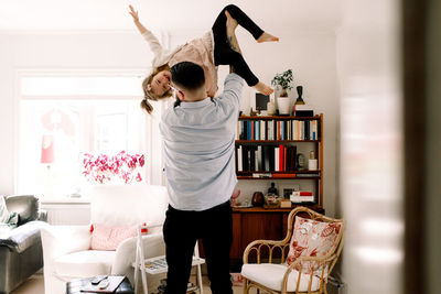 Rear view of playful father lifting cheerful daughter in living room at home