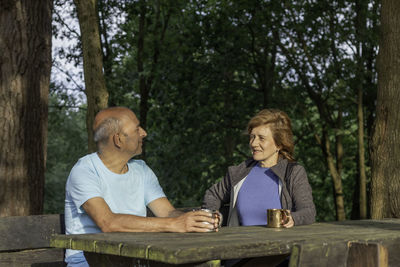 Senior couple looking to each other and smiling while sitting on a picnic wooden table resting