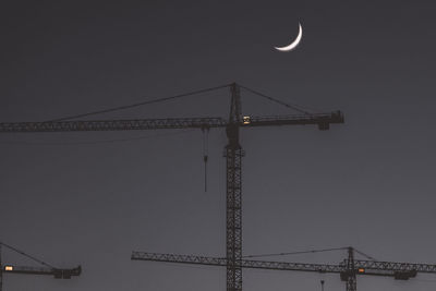Low angle view of silhouette cranes against sky at dusk