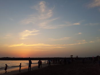 Tourists on beach against cloudy sky at sunset