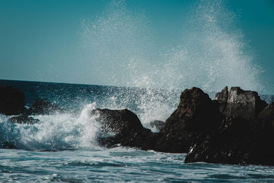 Waves splashing on rocks against sky