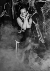 Young woman in costume sitting in spooky room during halloween