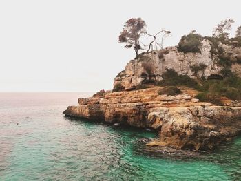 Rock formations by sea against clear sky