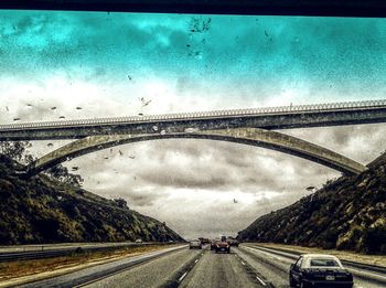 Cars moving on road against cloudy sky