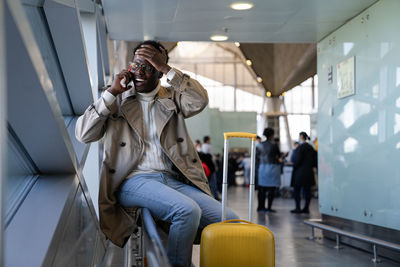 Black man shocked talking oncellphone sitting in airport, makes facepalm, forgot something important