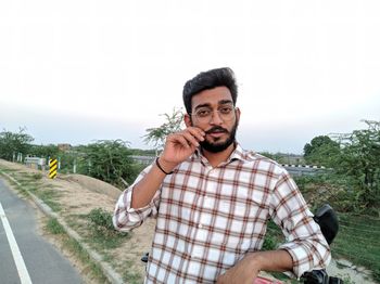 Portrait of young man standing on road against sky