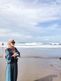 Woman wearing mask standing at beach against sky