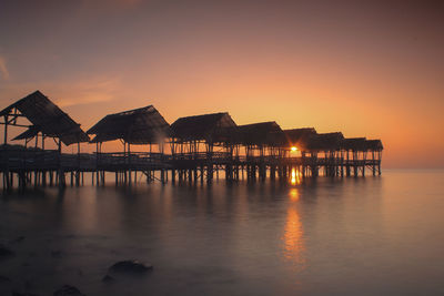 Silhouette huts over sea against sky