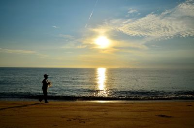 Man walking at beach against sky during sunset