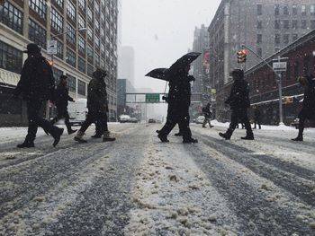 People walking on snowcapped street during snowfall in city
