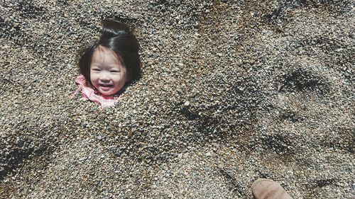 High angle portrait of cute girl covered with stones at beach