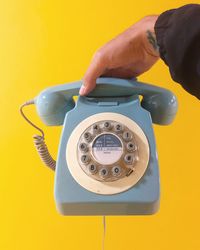 Cropped hand of woman holding telephone against yellow background