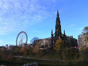 Ferris wheel by buildings against blue sky