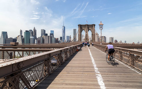 Rear view of woman cycling on brooklyn bridge in city against sky