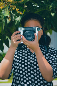A girl wearing a polkadot dress holding an slr camera obscuring her face 