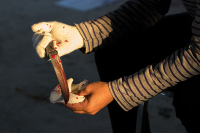 Midsection of criminal wiping blooded knife while sitting indoors