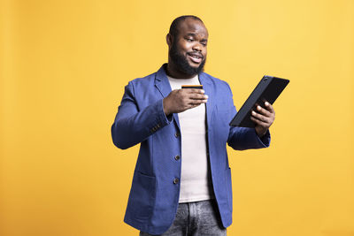 Young man using digital tablet while standing against yellow background