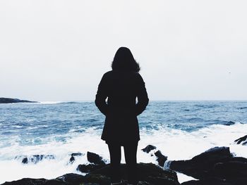 Rear view of woman standing on rock at shore against sky