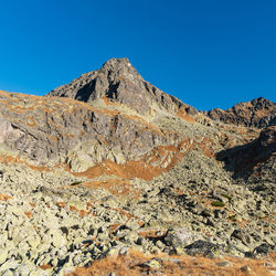 Low angle view of rocky mountain against clear blue sky