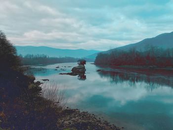 Scenic view of lake by mountains against cloudy sky