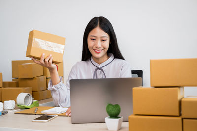 Cheerful woman holding parcels while sitting at office