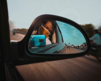 Reflection of man on side-view mirror of car