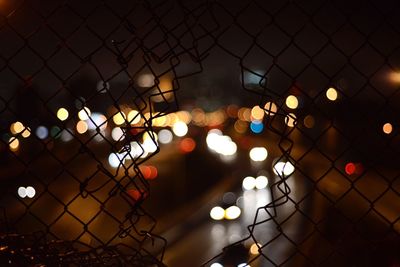 Illuminated lights seen through broken metal fence at night