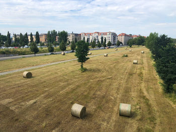 Hay bale field against sky in a city with buildings behind.