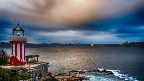 Lighthouse by sea against sky during sunset