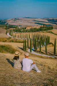 Rear view of men sitting on field against sky