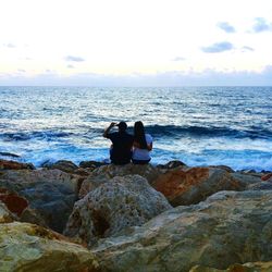 Rear view of people photographing sea against sky during sunset