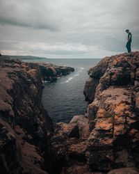 Man standing on rock formation by sea against sky