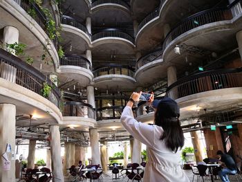 Rear view of woman photographing while standing in building