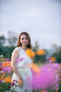 Portrait of smiling young woman standing against pink flowering plants