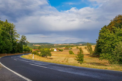 Empty road along trees and plants against sky