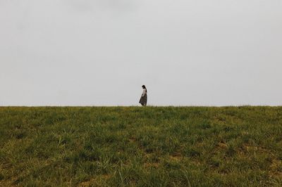 Mid distance view of woman on grassy field against clear sky