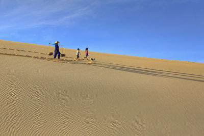 Rear view of men on sand dune in desert against sky