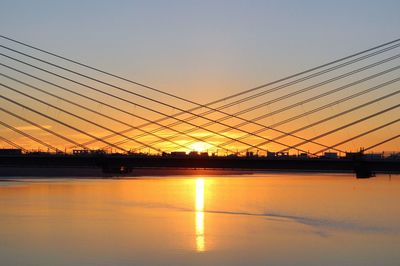 Silhouette bridge over city against sky during sunset