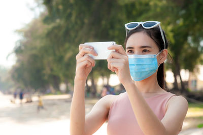 Young woman wearing mask photographing with smart phone at beach