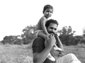 Portrait of baby girl with father sitting against sky