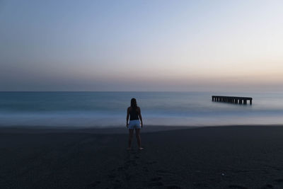 Rear view of woman standing on beach against clear sky