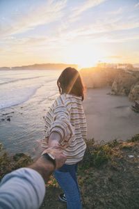 Cropped hand of man holding woman hand on cliff by beach