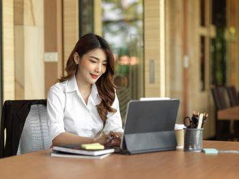 Young woman using mobile phone while sitting on table