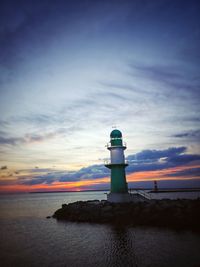Lighthouse by sea against sky during sunset