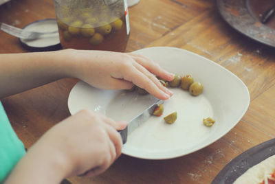 Cropped hand of woman cutting olives in plate on table