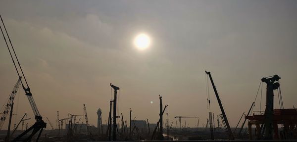 Silhouette cranes at harbor against sky during sunset